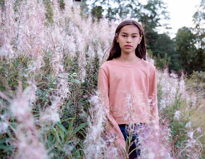 Flicka med mörkt hår som står på en blomstrande äng