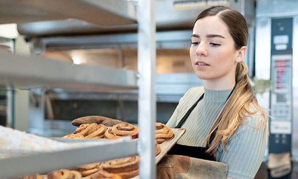 Kvinna i bageri som lägger en plåt med bullar i en ställning