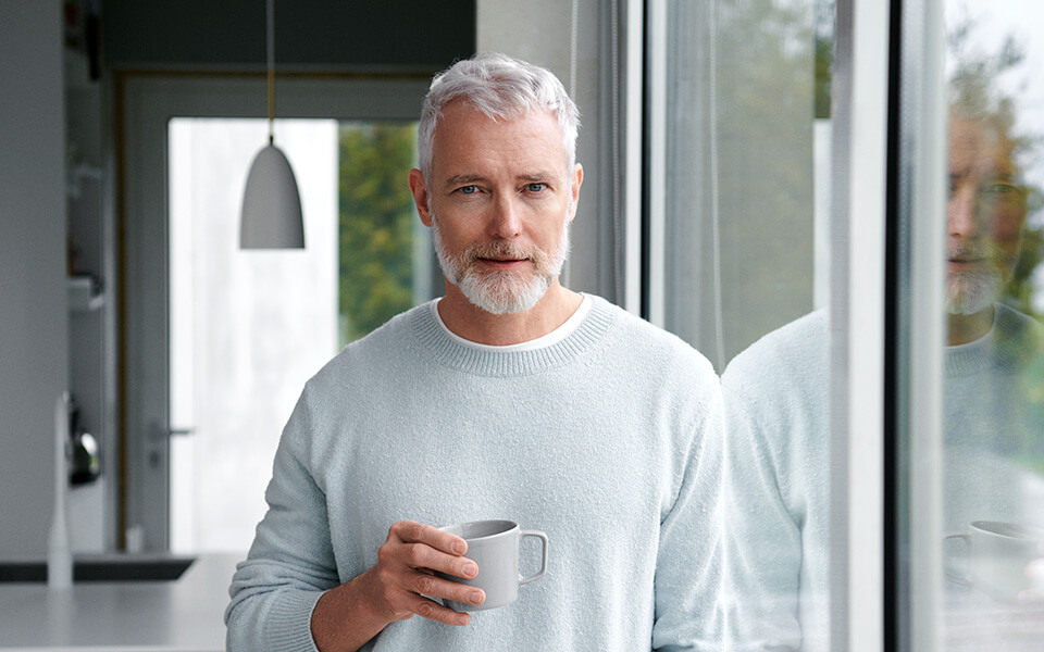 Man med kaffekopp tittar in i kameran.