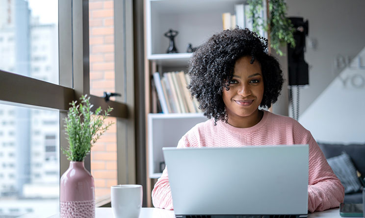 Kvinna som sitter vid ett skrivbord hemma framför en laptop