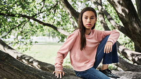 En flicka i rosa tröja sitter på trädet.